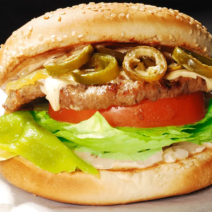 Char broiled burger with melted cheese, jalapeños, yellow chiles, lettuce and tomato on a seeded bun
