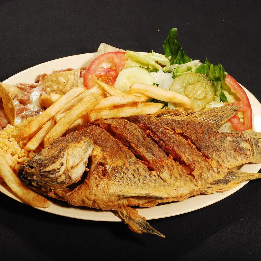 Whole fried mojarra on a plate with rice, fries and a green salad