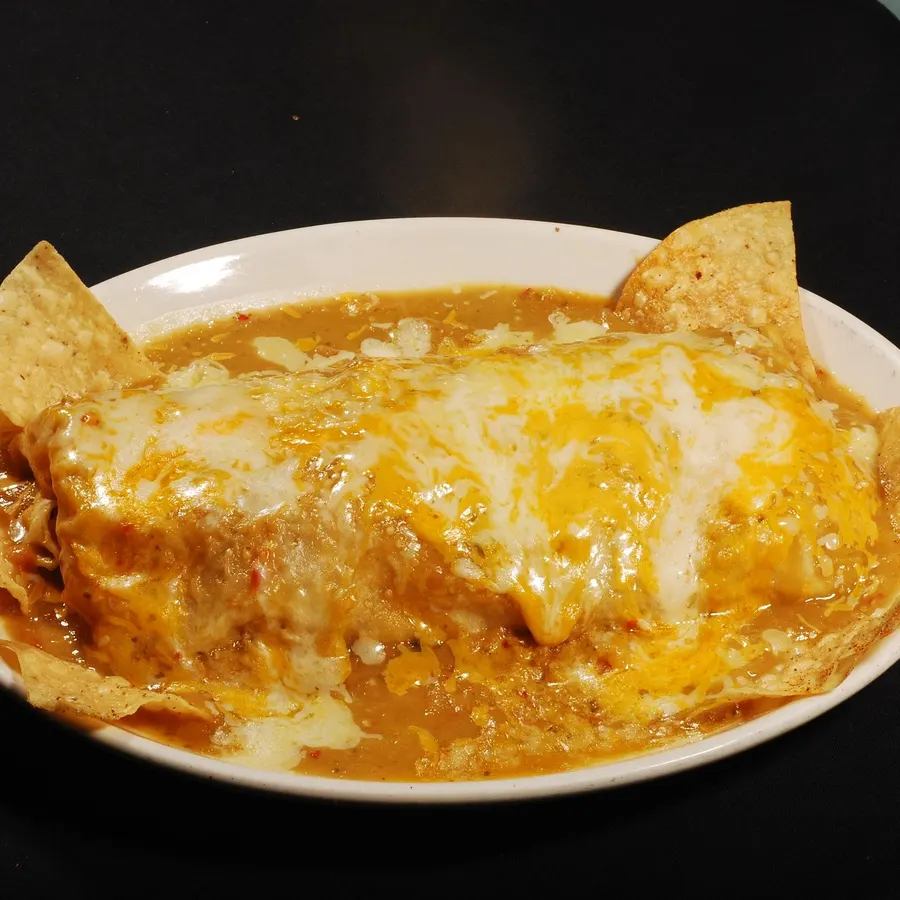 Wet burrito smothered in sauce and melted cheese, tortilla chips around the plate