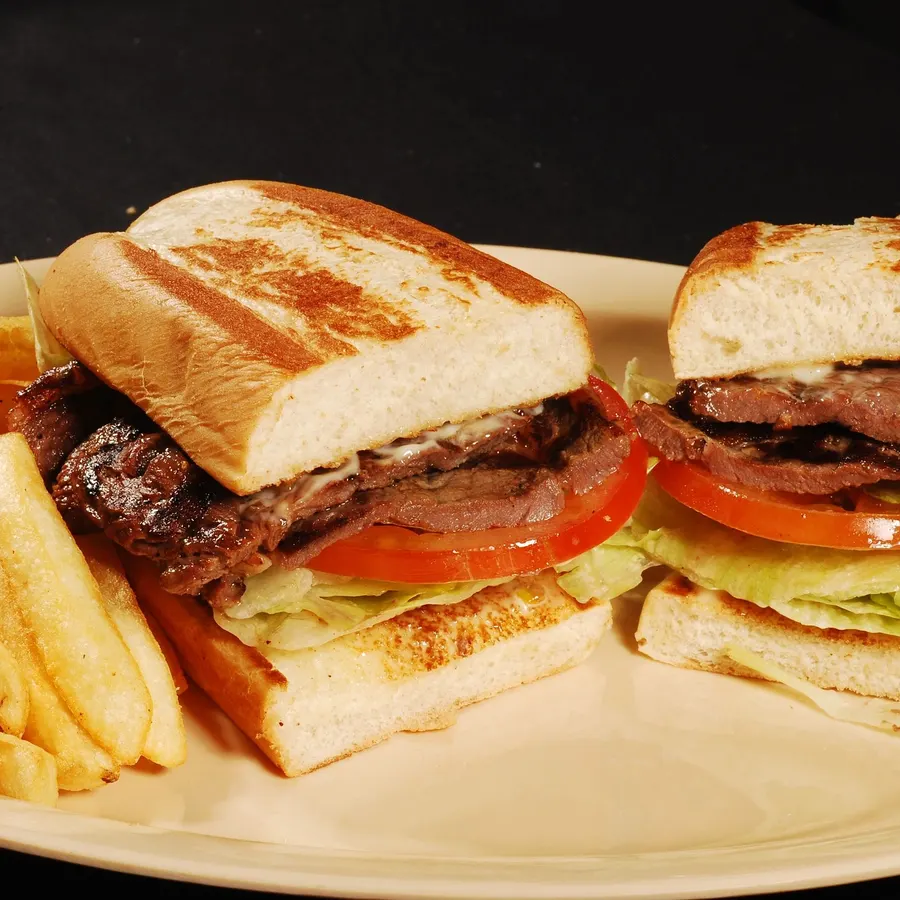 Steak sandwich on grilled bread with lettuce and tomato, fries alongside